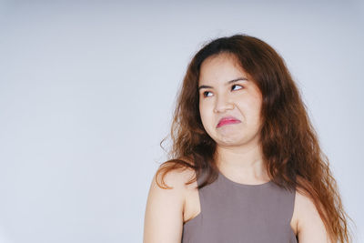 Young woman making face while standing against gray background