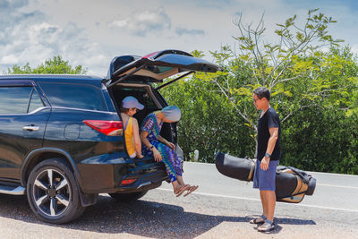 Two happy woman sitting at the car trunk on a road trip