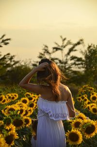 Woman standing on sunflower field against sky