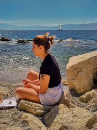 Woman sitting on rock at beach against sky