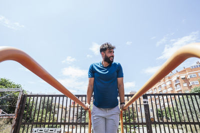 Portrait of young man standing against railing against sky