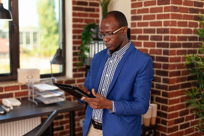 Side view of man using mobile phone while standing against wall