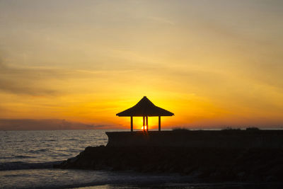 Silhouette lifeguard hut on beach against sky during sunset