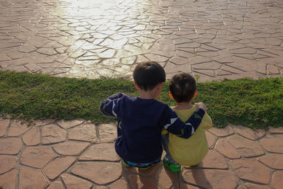 Rear view of siblings crouching on footpath