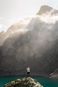 Man standing on rock by mountains against sky