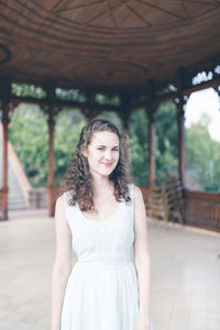 Beautiful curly hair girl in a light blue simple dress in a pavilion in a garden