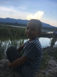 Boy sitting on land against sky