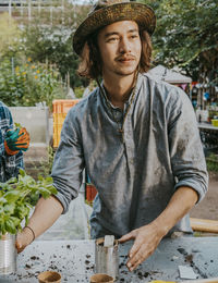Young male farmer with plant looking away in community garden