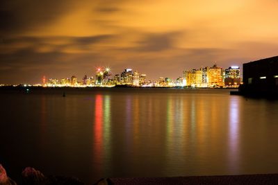 Illuminated cityscape by sea against sky at sunset