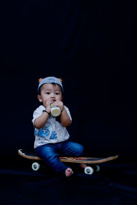 Portrait of cute girl holding baby while sitting against black background