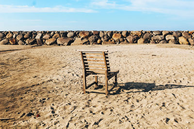 Deck chairs on rocks at beach against sky