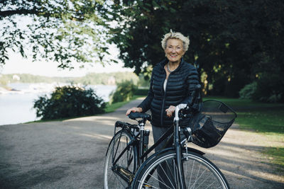 Portrait of smiling senior woman with bicycle in park