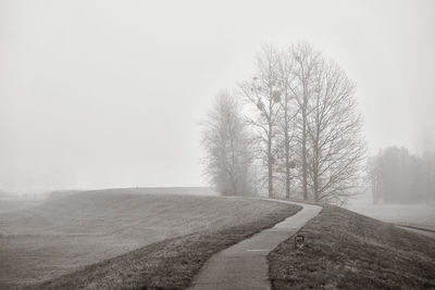 Road amidst bare trees on field against sky