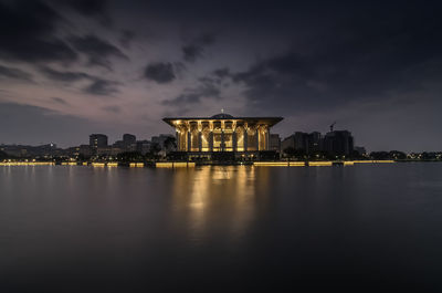 Illuminated iron mosque and lake against cloudy sky during sunrise