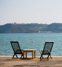 Deck chairs by sea against clear sky