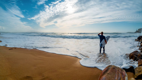 Man carrying surfboards while standing at beach against sky