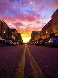 Cars on road amidst buildings against sky at sunset