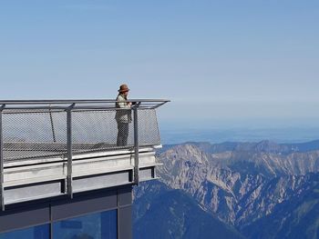Man looking at railing on mountain against sky