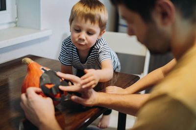 Preparing for halloween celebration.man with son drawing out eyes on a pumpkin to make jack lantern.