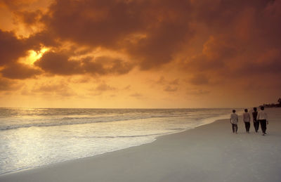 Silhouette people at beach against sky during sunset