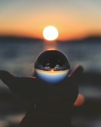 Close-up of hand holding sea against sunset sky