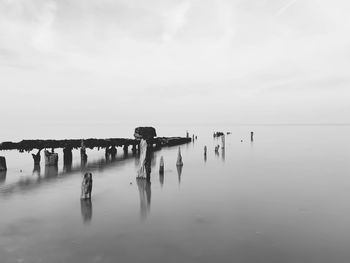 Wooden posts in sea against sky