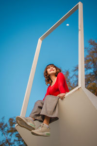 Portrait of smiling young woman standing against blue sky
