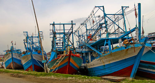 Fishing boats moored at harbor against sky