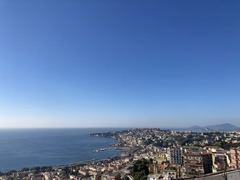 Aerial view of townscape by sea against clear blue sky