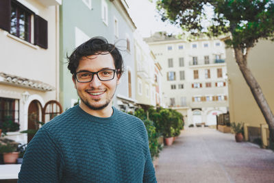 Portrait of smiling young man standing against buildings in city