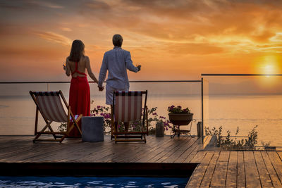 Rear view of people standing by sea against sky during sunset