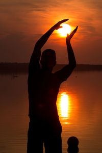 Silhouette woman standing by sea against sky during sunset