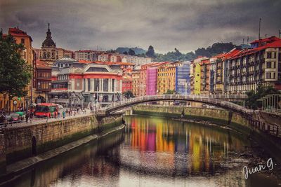 Bridge over river by buildings in city against sky