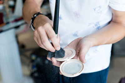 Midsection of make-up artist holding compact powder and brush