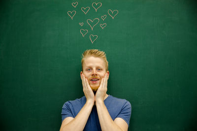 Smiling young man gesturing with heart shapes on blackboard