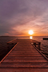 Wooden pier over sea against dramatic sky during sunset