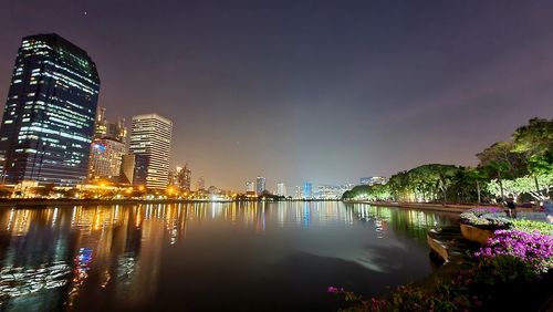 Illuminated buildings by river against sky at night