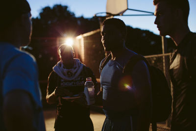 Friends discussing while standing in basketball court at dusk