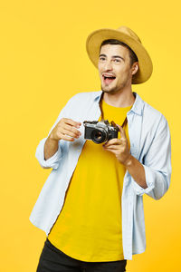 Happy young man photographing against yellow background