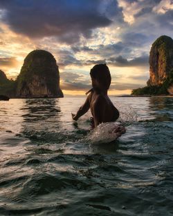 Woman in sea by rocks against sky