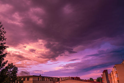 Low angle view of buildings against dramatic sky during sunset