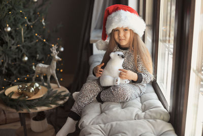 Portrait of cute girl sitting by window during christmas