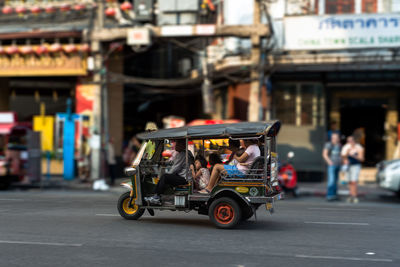 People travelling in jinrikisha on street against buildings