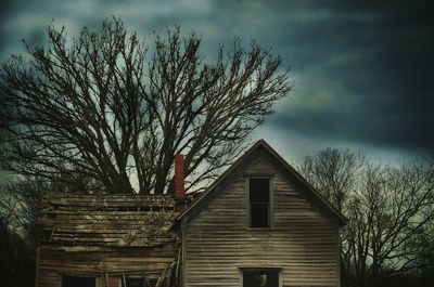 Low angle view of bare trees against cloudy sky