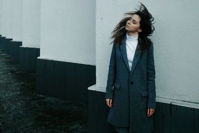 Beautiful young woman standing against wall