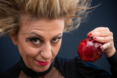 Portrait of woman holding apple against black background