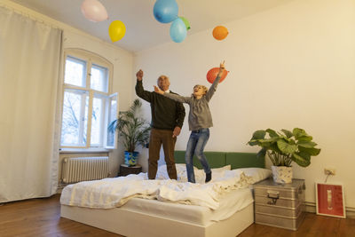 Happy grandfather and grandson playing with balloons on bed at home