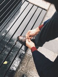 Low section of man tying shoelace on wet bench during rainy season