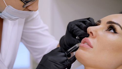 Medical office, doctor in black sterile gloves, injecting hyaluronic acid into the patient lips. 