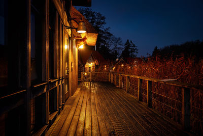 Empty footpath amidst illuminated buildings at night